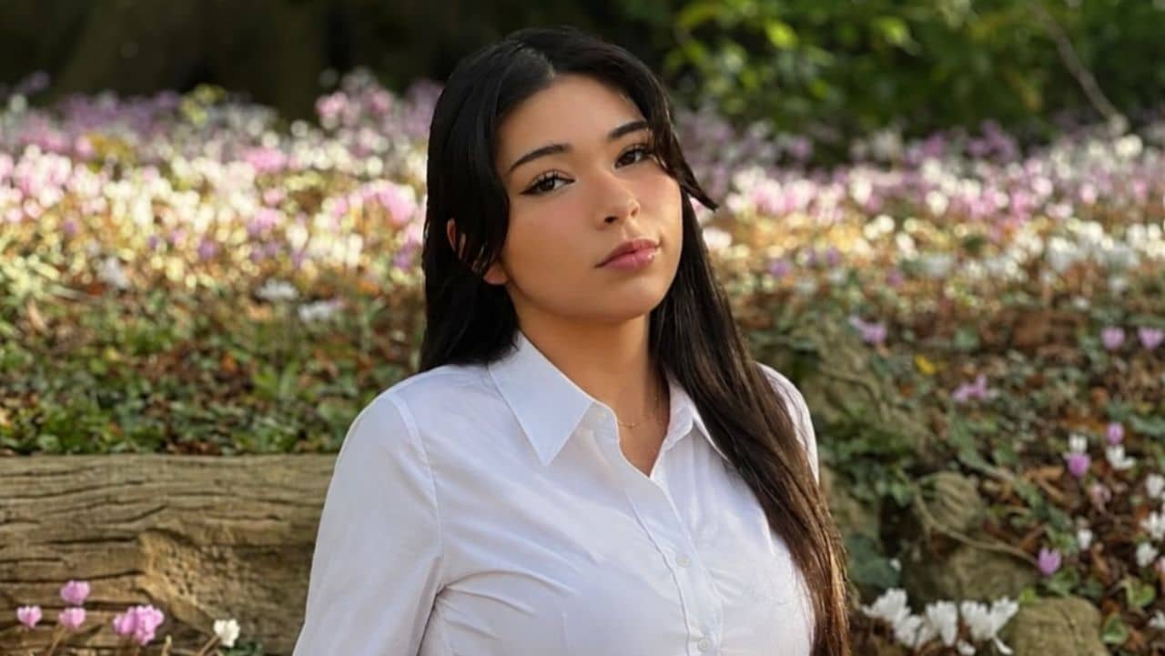 Aishah Sofey highlights timeless elegance with a crisp white button-down shirt set against a lush floral garden backdrop, creating a clean and sophisticated minimalist aesthetic.