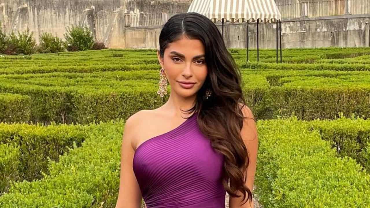 Amanda Trivizas pairs a textured deep violet one-shoulder mini dress with statement gold and jewel earrings for a timeless and elegant daytime event look.