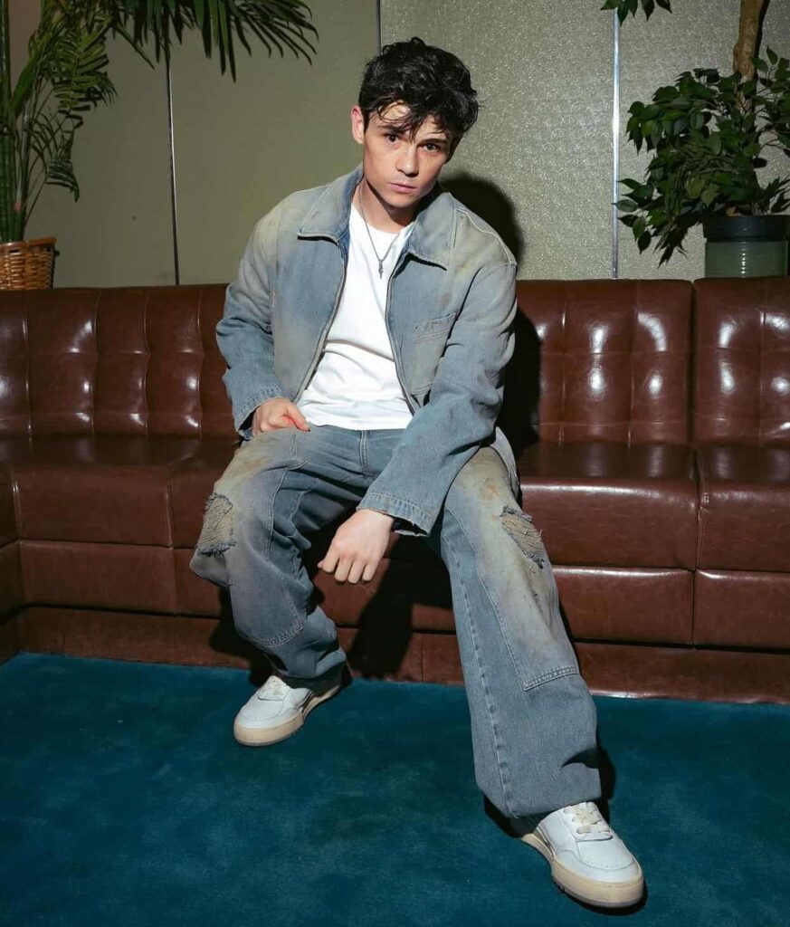 Ashby Gentry leans into a vintage grunge aesthetic with a distressed double-denim set featuring relaxed distressed jeans, a matching faded jacket, a crisp white tee, and clean leather sneakers.