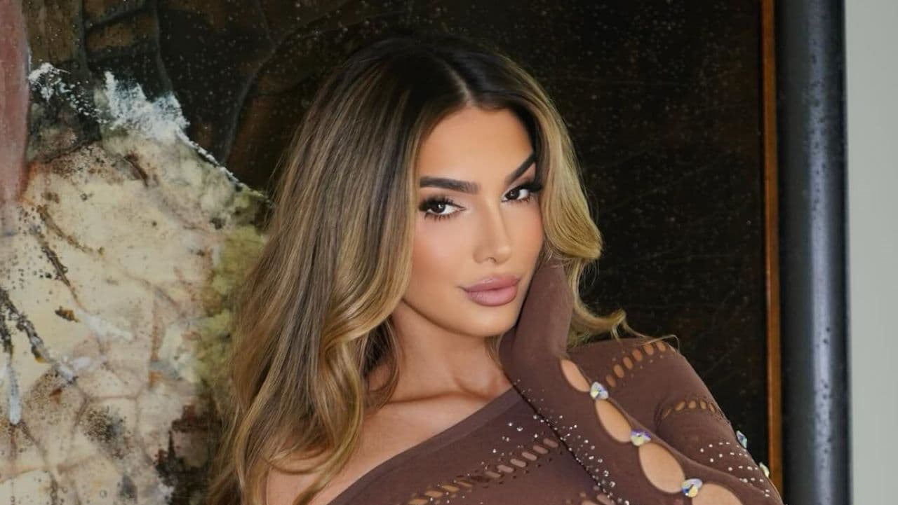 Lyna Perez effortlessly showcases modern glamour in a chic, earth-toned top featuring intricate cut-out sleeves and subtle rhinestone embellishments that perfectly complement her warm caramel balayage.
