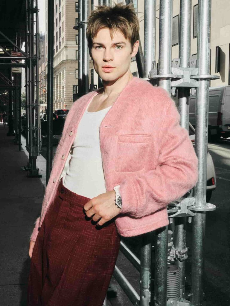 Showcasing a chic contemporary menswear look, Noah LaLonde pairs a plush pastel pink cardigan with tailored burgundy plaid trousers for an elevated urban ensemble.