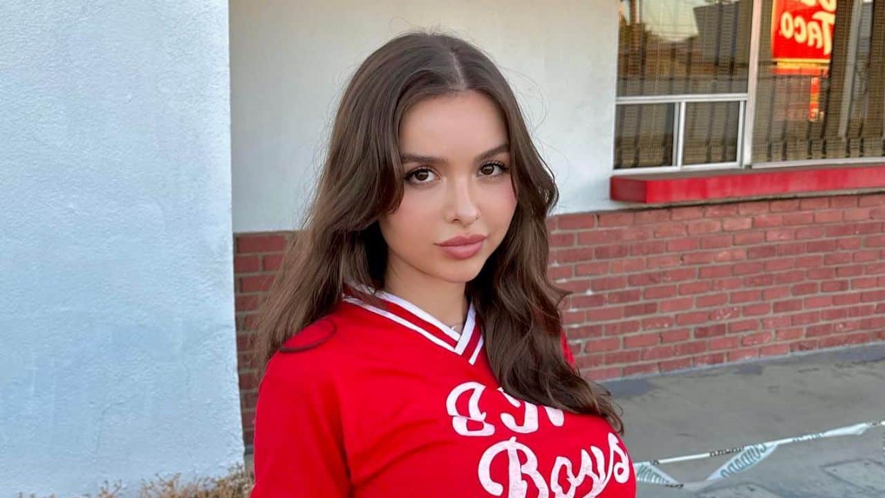 Sophie Mudd brings a playful, laid-back vibe to urban street style with a sporty red varsity-inspired top and soft, cascading waves.