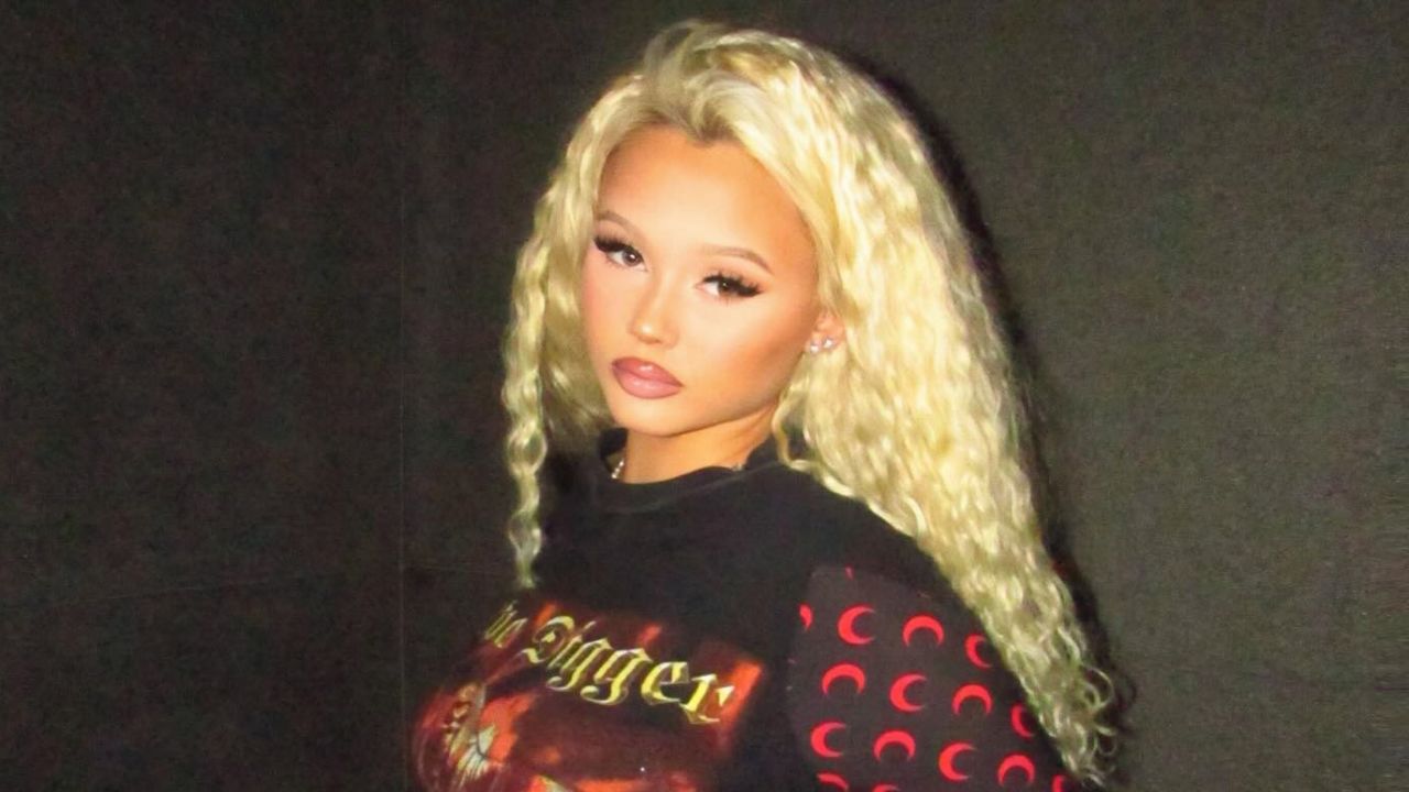 Alabama Barker embraces a bold streetwear vibe, combining a graphic graphic-print top with signature crimped platinum waves and flawless glam makeup.