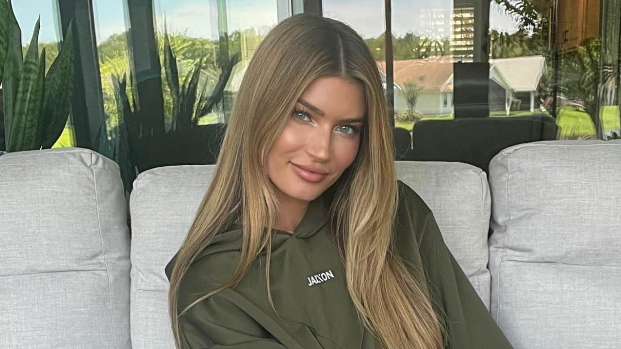 Hayley Maxfield strikes a cozy, confident pose in a casual yet stylish olive green cotton hoodie featuring subtle 'JAXON' chest embroidery, her long blonde hair styled in beachy waves.