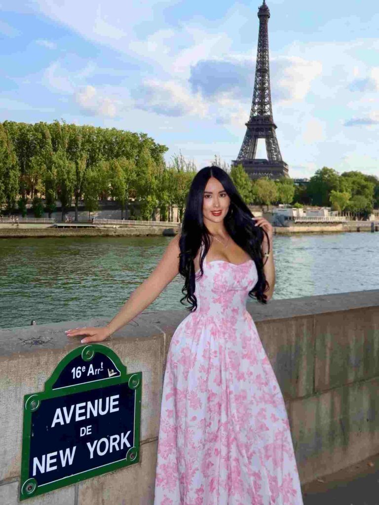 Posing along the Parisian waterfront, Kate Carvajal exudes effortless romantic charm in a flowing white and pink floral sundress with an iconic Eiffel Tower view.
