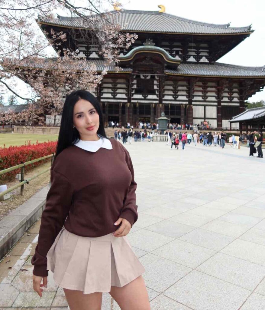 Kate Carvajal channels a timeless preppy aesthetic by layering a rich chocolate-brown pullover over a crisp white collar, seamlessly paired with a pleated beige mini skirt.