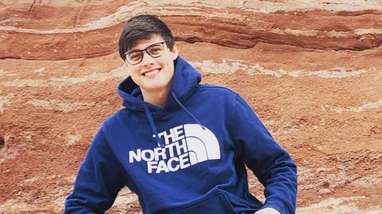Landon Clifford effortlessly combines casual comfort with outdoor-inspired style, sporting a branded hoodie and trendy glasses against a striking red rock formation.