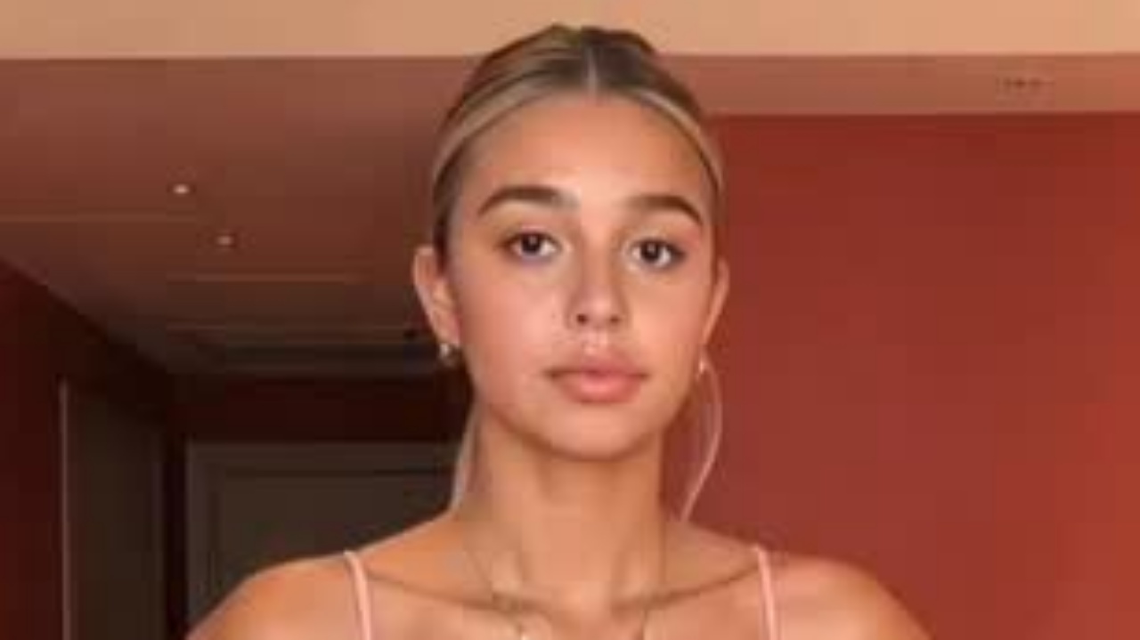 Lily Nador effortlessly embraces modern minimalism by pairing a delicate blush-pink strap top with dainty layered gold jewelry and a sleek, polished updo.