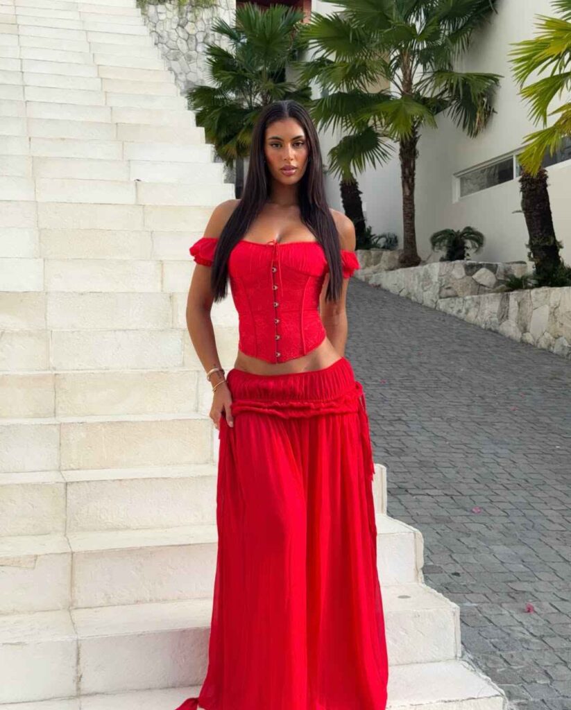 Mia Bailey makes a stunning fashion statement in a bold, all-red ensemble, combining an off-the-shoulder corset top with a sweeping maxi skirt for a dramatic summer appearance.