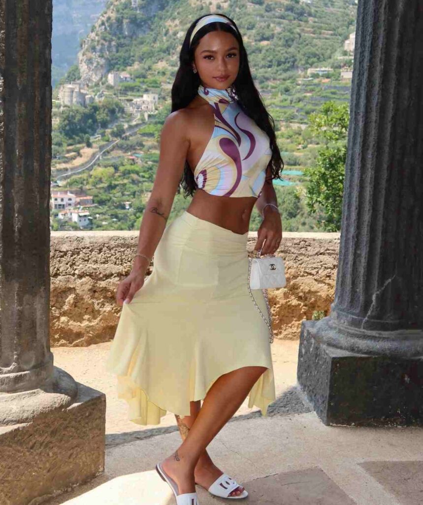 Saby Tuts channels ultimate European resort glamour in a retro abstract-swirl halter crop top and matching headband, beautifully balanced with a breezy pastel yellow midi skirt and a luxury white quilted handbag.