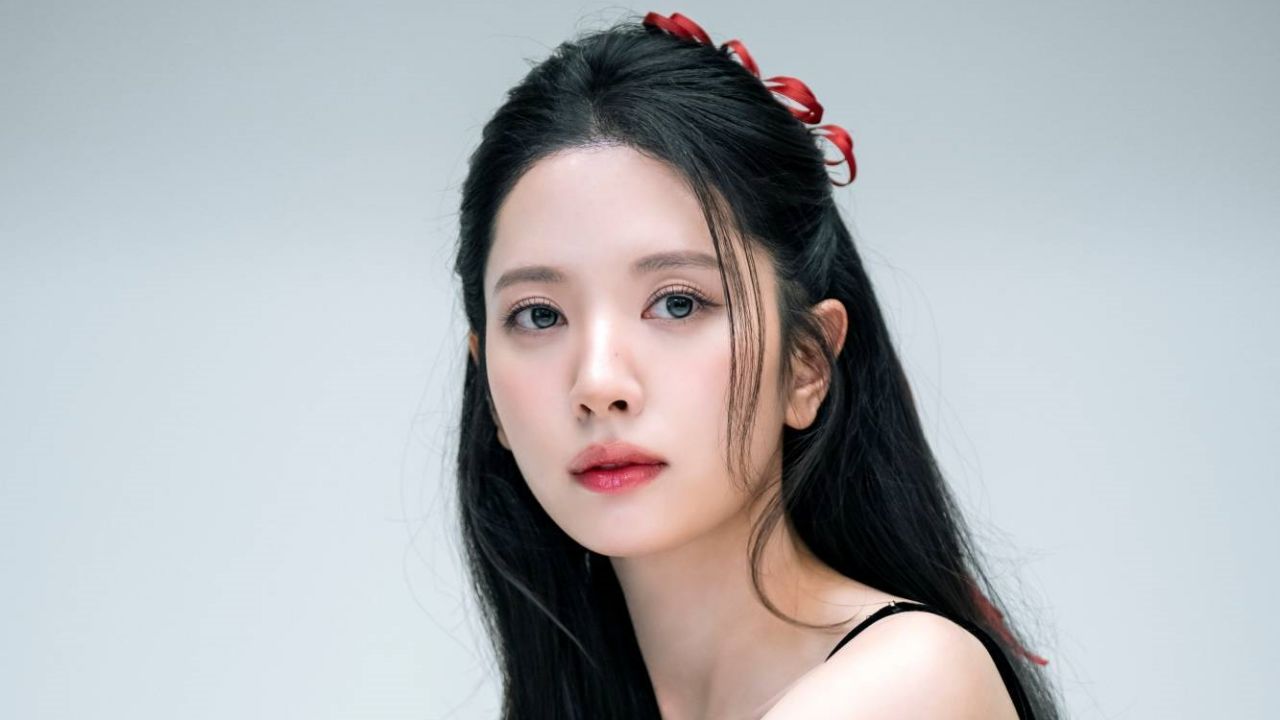 Bona embodies effortless grace with radiant, dewy makeup and a delicate red ribbon woven into her hair, adding a subtle romantic accent to her sleek, minimalist black ensemble.