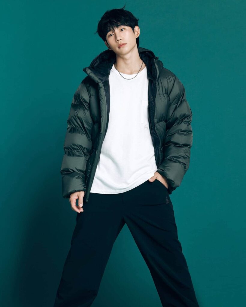 Hae In perfectly captures cozy street style, layering a striking deep forest green puffer jacket over a casual white tee and relaxed black trousers.
