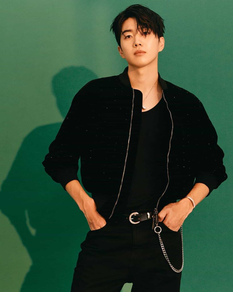 Kang Hoon commands attention in a sleek, monochromatic smart-casual look featuring a subtly textured black bomber jacket elevated by polished silver hardware accents.