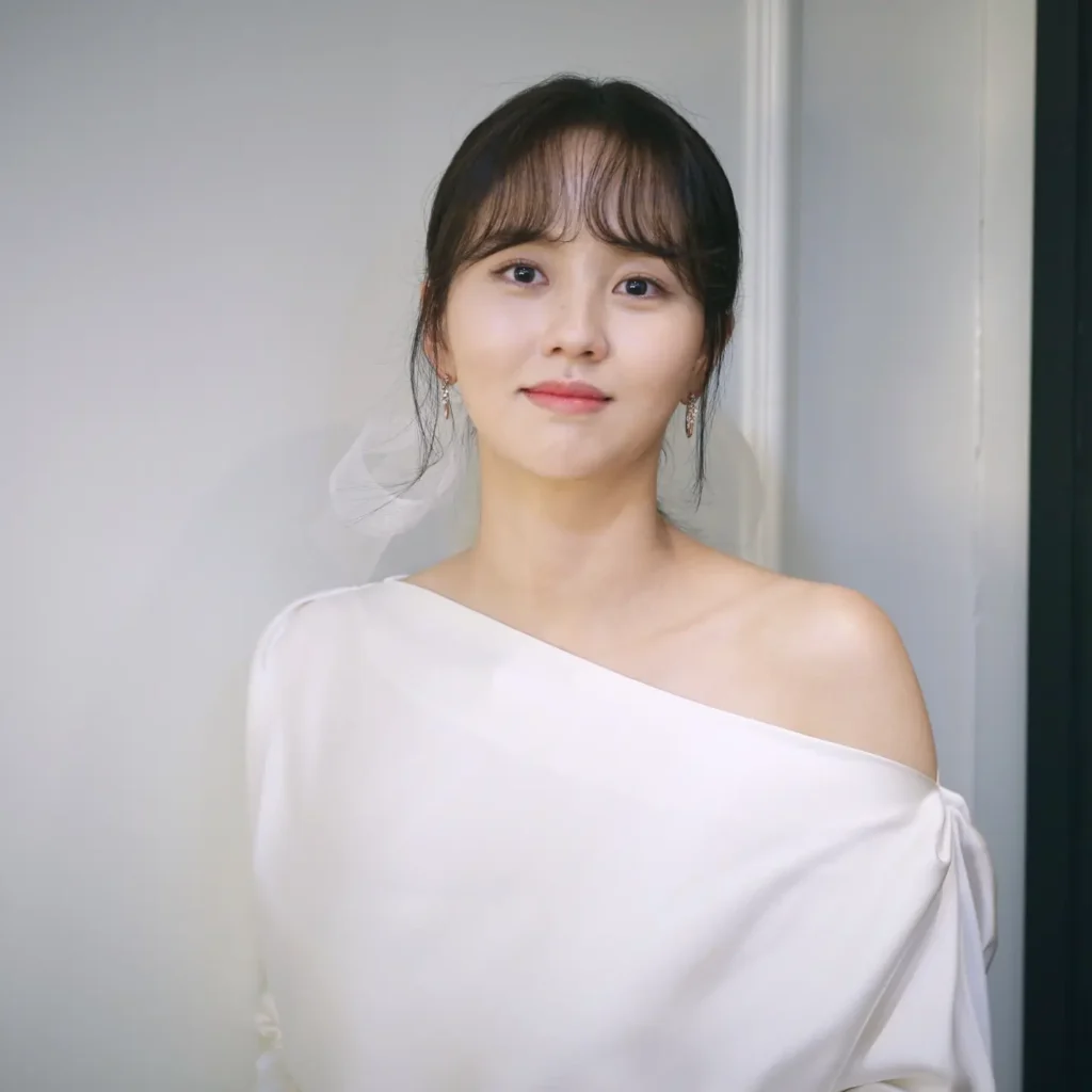 Exuding timeless romantic elegance, Kim So Hyun turns heads in an ethereal off-the-shoulder draped white satin silhouette styled with a soft fringed updo and delicate drop earrings.