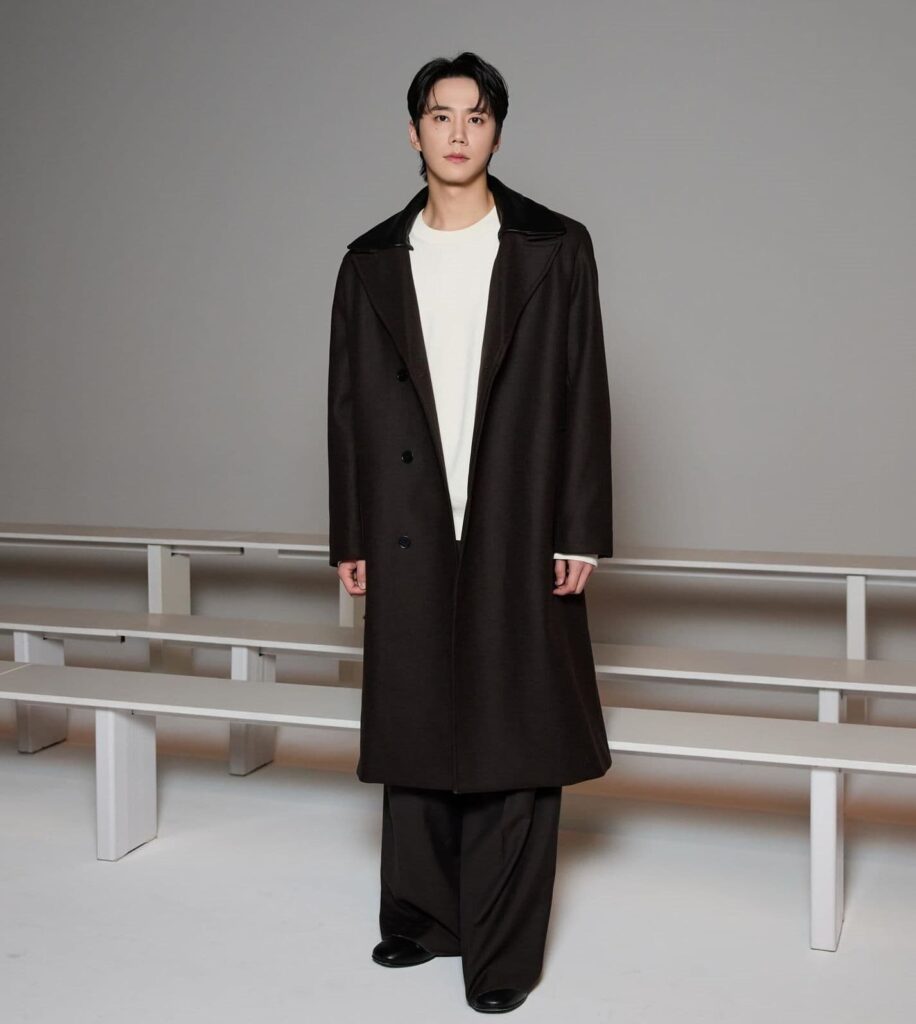 Lee Jun Young commands front-row allure by contrasting a structured dark wool overcoat and fluid wide-leg trousers with a crisp, minimalist base layer.