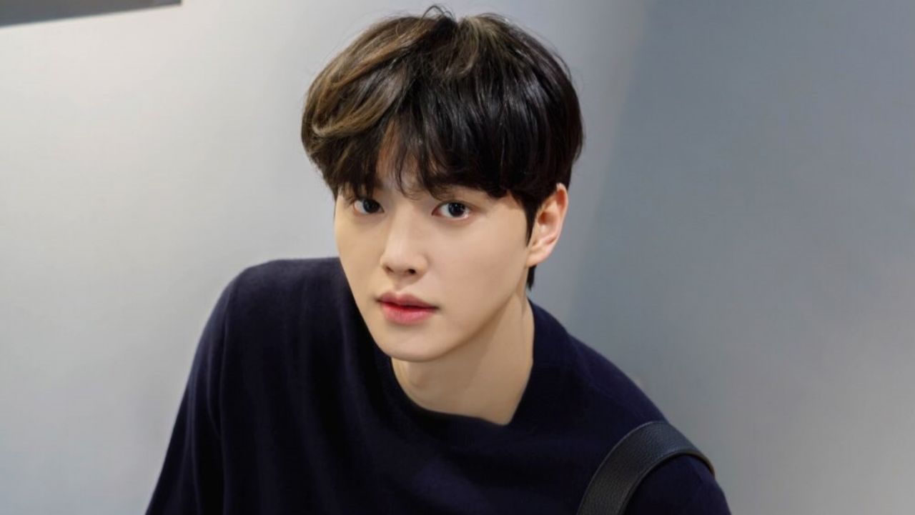 Song Kang effortlessly embodies modern minimalist style with an oversized navy blue crewneck sweater, paired with a sleek leather strap bag for a clean, sophisticated casual look.