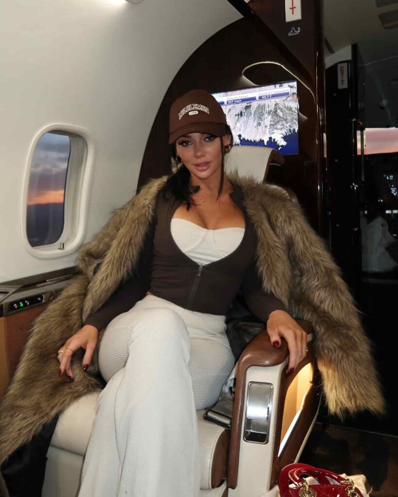 Stassi Wilde elevates luxury travel style, layering a statement faux fur coat over comfortable ribbed lounge pants and a branded baseball cap for a sophisticated yet effortless on-the-go look.