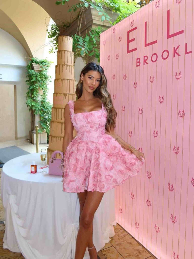 Embracing romantic cocktail chic, Tiffany Keller stuns in a blush pink 3D rosette mini dress beautifully styled with delicate gold jewelry and a pastel designer handbag.
