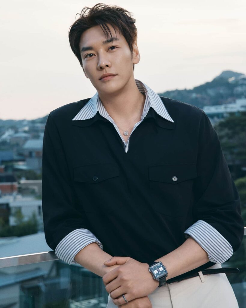Kim Young Kwang demonstrates high-end smart-casual layering by pairing a structured black overshirt with classic striped accents, sharply elevated by tailored neutral trousers and a luxury square timepiece.